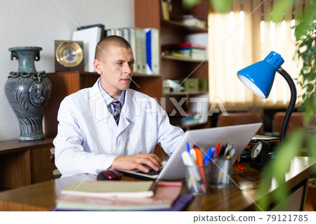Man doctor sitting in office at workplace Man doctor sitting in office at workplace 79121785