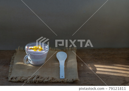 Vegan soy strawberry yogurt sprinkle with ripe sweet corn kernels in glass and white spoon over sackcloth and old wooden table. 79121811