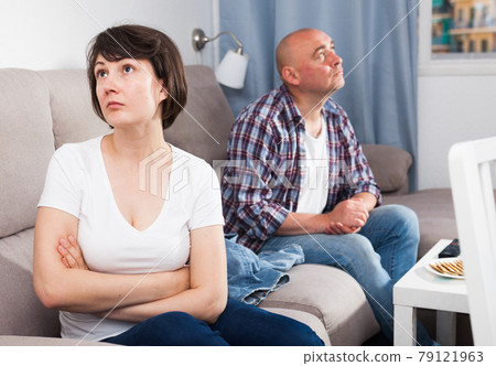 Upset mature woman sitting, man quarrelling on background at home Upset mature woman sitting, man quarrelling on background at home 79121963
