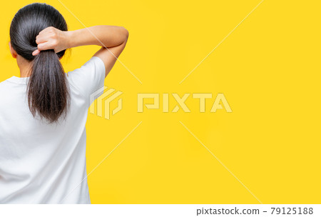 Back view of Asian woman holding damaged hair on yellow background with copy space. Split ends hair problem in woman. Dry and brittle black long hair needs shampoo and conditioner for spa treatment. 79125188