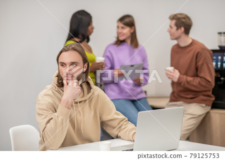 Thinking guy near laptop and colleagues chatting behind 79125753