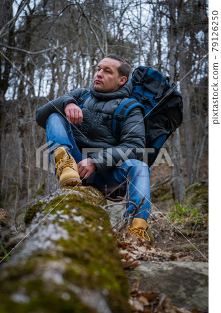 Hiker traveler sits on an old tree in a dense autumn forest Hiker traveler sits on an old tree in a dense autumn forest 79126250