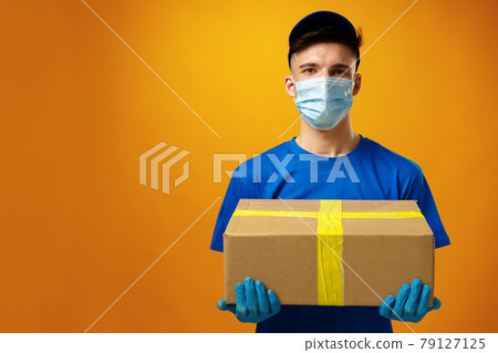 Young delivery man in face mask and gloves holding cardboard box parcel Young delivery man in face mask and gloves holding cardboard box parcel 79127125