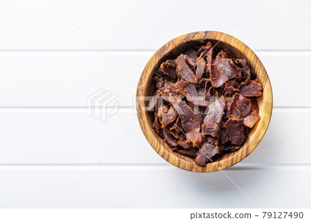 Sliced beef jerky. Dried beef meat in bowl on white table. Sliced beef jerky. Dried beef meat in bowl on white table. 79127490