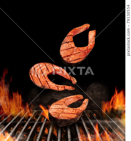 Grilled delicious salmon steaks are falling down on black background. Barbecue bbq grill, flaming fire, ember charcoal and smoke. Seafood. Close up 79130554