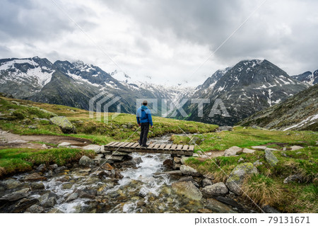 Man hiker resting on small bridge over mountaian river at Schlegeis Lake, Zillertal Alps, Austria Man hiker resting on small bridge over mountaian river at Schlegeis Lake, Zillertal Alps, Austria 79131671
