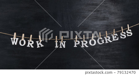 Words WORK IN PROGRESS with clothespins on black background. Phrase from white letters 79132470