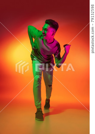 Portrait of Caucasian young man dancing, dancing isolated on orange studio background in neon light. Concept of human emotions, facial expression. Portrait of Caucasian young man dancing, dancing isolated on orange studio background in neon light. Concept of human emotions, facial expression. 79132598