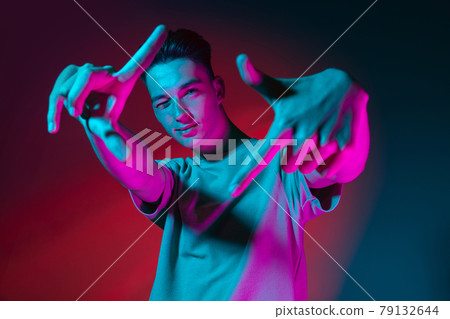 Gesturing. Portrait of Caucasian young man posing isolated on dark red studio background in neon pink light. Concept of human emotions, facial expression. Gesturing. Portrait of Caucasian young man posing isolated on dark red studio background in neon pink light. Concept of human emotions, facial expression. 79132644