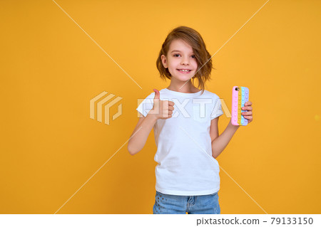 Little girl holding telephone and show thumb up isolated over yellow color background 79133150
