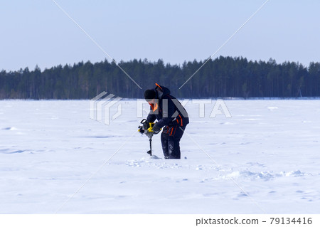 fisherman on a winter lake drills the ice with a motor drill fisherman on a winter lake drills the ice with a motor drill 79134416