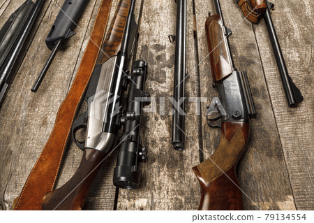 Many hunting rifles on weathered wooden surface 79134554
