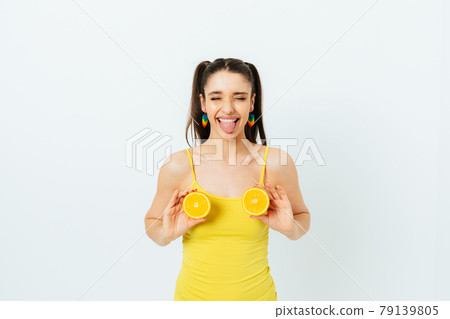 Playful young woman wearing yellow summer top holds orange halves 79139805