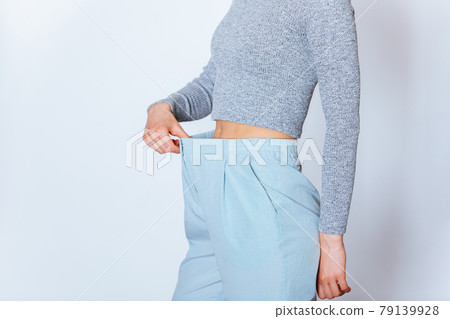 Weight loss concept, slim young woman pulling off oversized pants Weight loss concept, slim young woman pulling off oversized pants 79139928