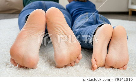 Closeup of mother and son lying on floor and showing bare feet. Family having fun and playing together Closeup of mother and son lying on floor and showing bare feet. Family having fun and playing together 79141810