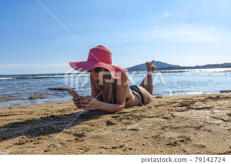 woman in black bikini and red hat lying on tropical beach 79142724