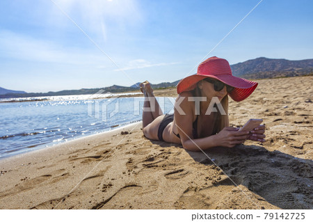 woman in black bikini and red hat lying on tropical beach 79142725