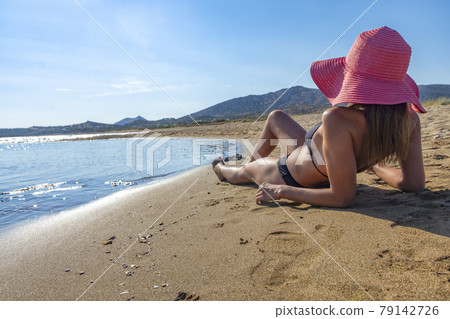 rear view of a woman in black bikini and red hat lying on tropical beach 79142726