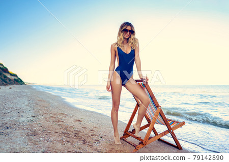 A young woman in a swimsuit relaxing on a deckchair on the beach A young woman in a swimsuit relaxing on a deckchair on the beach 79142890