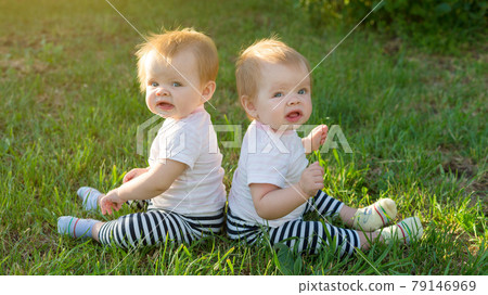 The twins are sitting on the green grass on a sunny day in the city park The twins are sitting on the green grass on a sunny day in the city park 79146969