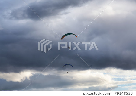 Adventurous Man Flying on a Paraglider around the mountains. 79148536