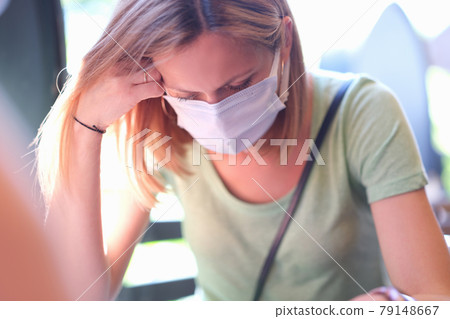 anxious sad woman in medical protective mask sits at table anxious sad woman in medical protective mask sits at table 79148667