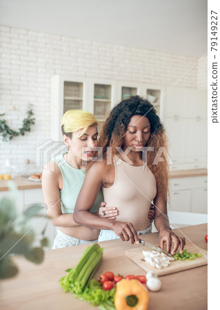 Caucasian woman holding dark-skinned cooking girlfriend by waist Caucasian woman holding dark-skinned cooking girlfriend by waist 79149227