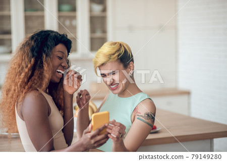 Two girlfriends looking into smartphone and laughing Two girlfriends looking into smartphone and laughing 79149280