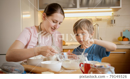 Happy mother with little son stirring and mixing dough ingredients in big glass bowl. Children cooking with parents, little chef, family having time together, domestic kitchen. Happy mother with little son stirring and mixing dough ingredients in big glass bowl. Children cooking with parents, little chef, family having time together, domestic kitchen. 79149326