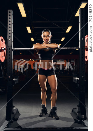 Charming woman standing and leaning on gym equipment 79149870