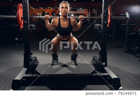 Strong female athlete doing squats with a barbell 79149871