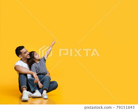 Cheerful arab dad and daughter pointing at copy space over yellow background 79151843