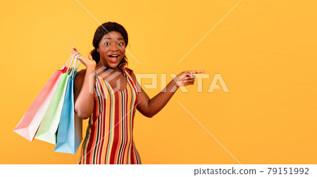 Excited black lady in dress holding shopper bags, cannot believe big sale, pointing at empty space on orange background Excited black lady in dress holding shopper bags, cannot believe big sale, pointing at empty space on orange background 79151992