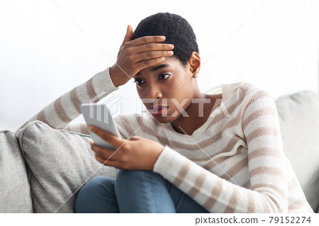 Concerned Black Lady Looking At Smartphone Screen At Home And Touching Head 79152274