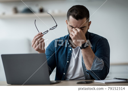 Tired young male feel pain eye strain hold glasses, rubbing dry irritated eyes Tired young male feel pain eye strain hold glasses, rubbing dry irritated eyes 79152314