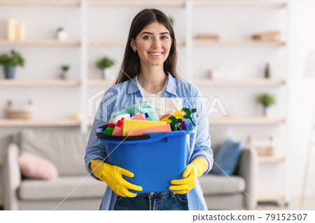 Cheerful young housewife holding bucket with cleaning supplies tools 79152507
