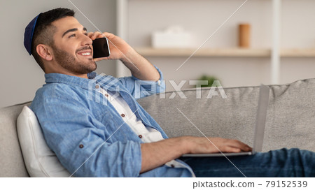 Smiling jew man working and talking on phone at home Smiling jew man working and talking on phone at home 79152539
