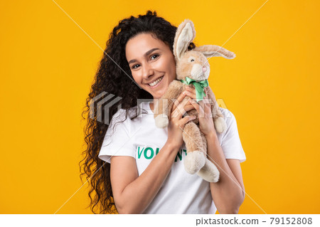 Female Volunteer Holding Bunny Toy Standing Posing Over Yellow Background 79152808