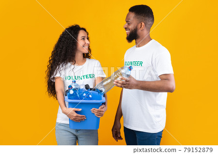 Two Diverse Volunteers Putting Plastic Bottle In Box, Yellow Background 79152879