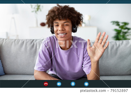 Head shot of black teenager in headphones waving hand to webcam, greeting teacher during online class, pc screen view Head shot of black teenager in headphones waving hand to webcam, greeting teacher during online class, pc screen view 79152897