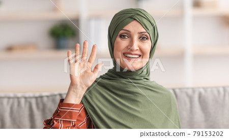 Happy Mature Muslim Lady In Hijab Waving Hand At Home Happy Mature Muslim Lady In Hijab Waving Hand At Home 79153202
