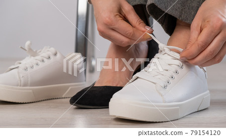 Close-up business woman takes off her shoes puts on white leather sneakers. 79154120