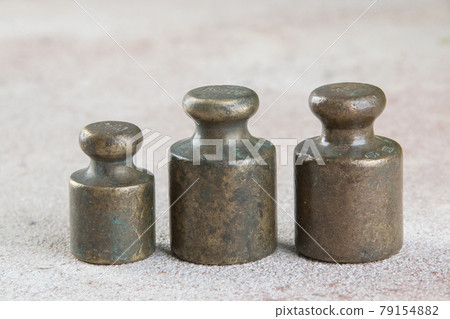 Three antique bronze weights for scales on concrete background. 79154882