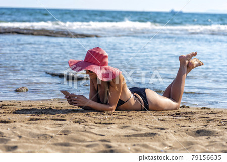 sexy mature woman in black bikini and red hat lying on tropical beach 79156635