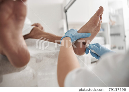 Careful podiatrist grinds heel of male client with modern tool at pedicure procedure in salon 79157596