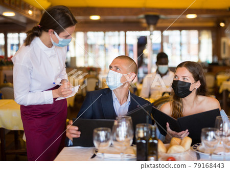 Woman waiter in protective mask is taking order from clients in restaurante 79168443