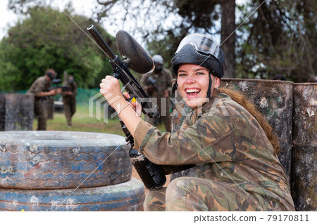 Paintball players of one team in camouflages and masks aiming with gun in shootout playing Paintball players of one team in camouflages and masks aiming with gun in shootout playing 79170811
