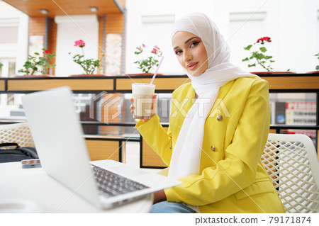 Beautiful young muslim woman using laptop while sitting in cafe Beautiful young muslim woman using laptop while sitting in cafe 79171874
