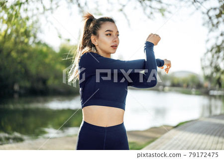 Fit young girl in dark blue sportswear exercising in park Fit young girl in dark blue sportswear exercising in park 79172475