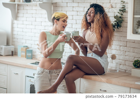 Laughing dark-skinned woman and caucasian girlfriend with cups Laughing dark-skinned woman and caucasian girlfriend with cups 79173634